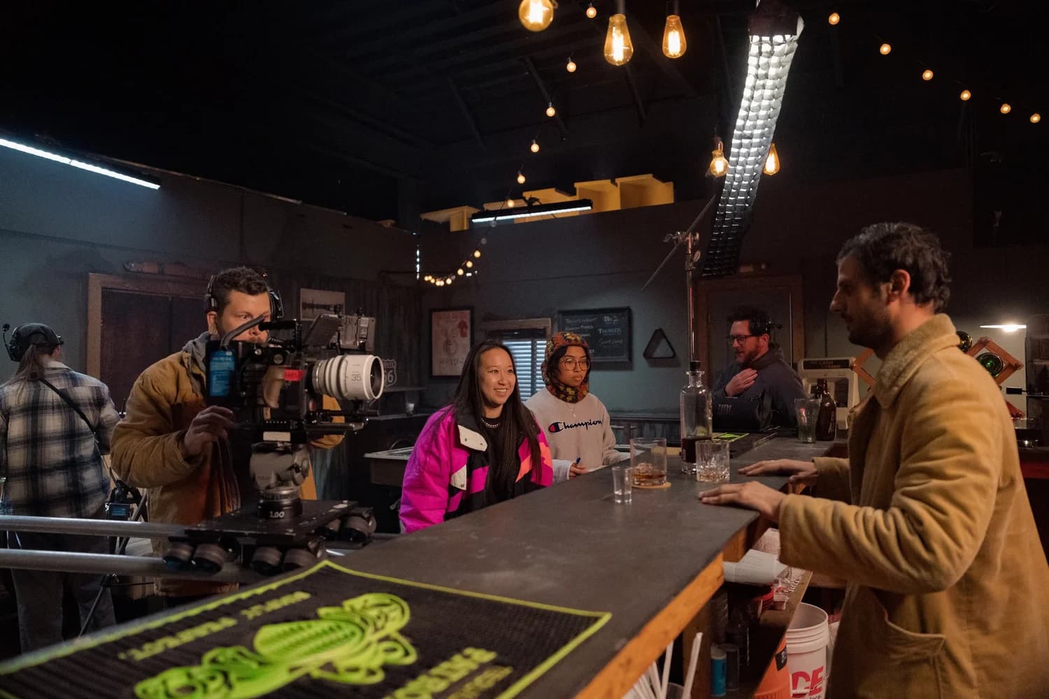 Olivia Wong on set behind a bar, watching a take, with the camera operator, crew and lighting rig around her