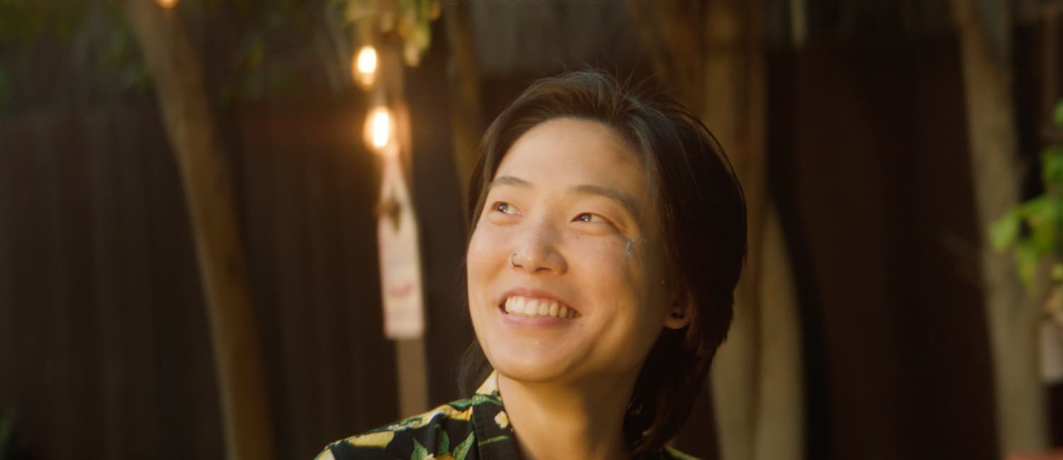 A person in a floral shirt smiling and looking upward, string lights strung behind them at golden hour — a still from the Republic Restoratives spec commercial
